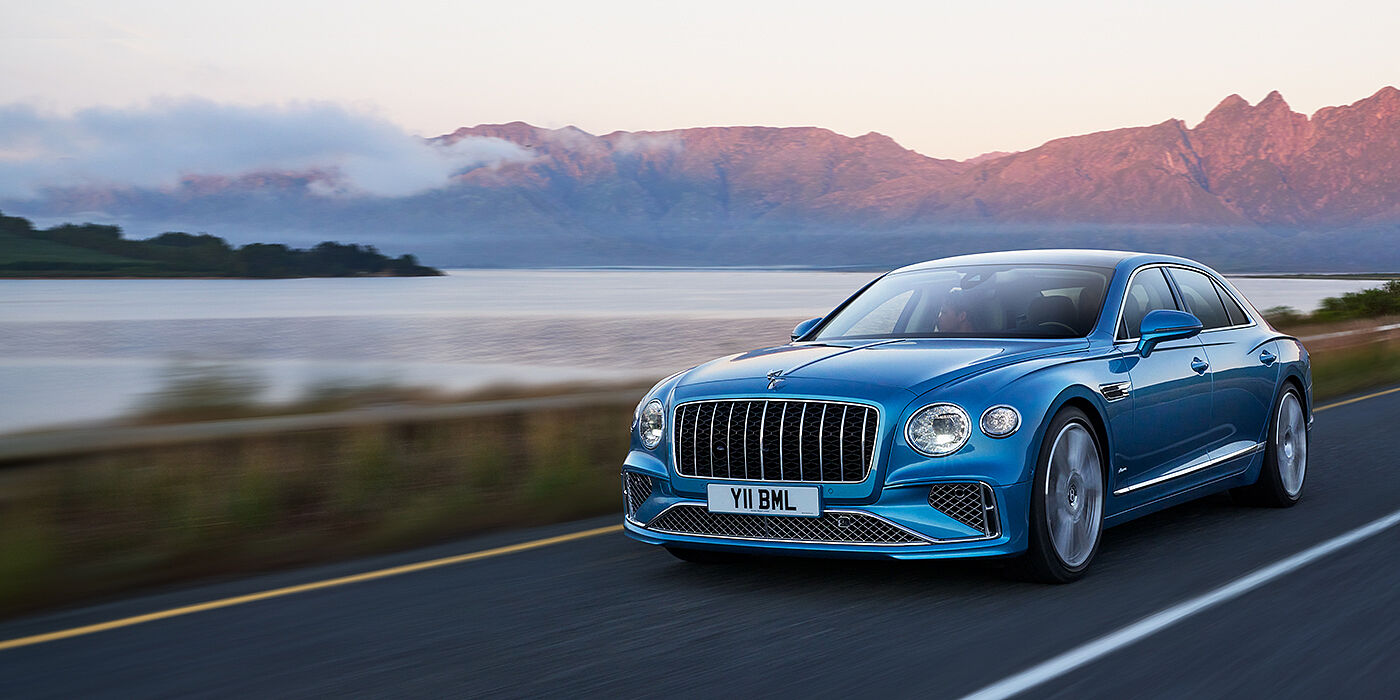 Bentley Edinburgh New Bentley Flying Spur Azure sedan in Light windsor blue paint by Mulliner, with 22 inch Azure wheels and chrome straight vaned grille driving on a mountain road