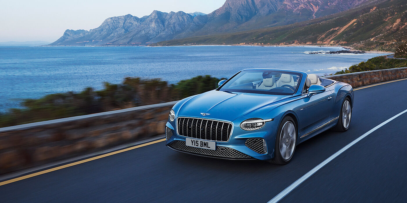 Bentley Edinburgh New Bentley Continental GTC Azure convertible in Light Windsor blue paint with 22 inch Azure wheels and chrome grill, driving dynamically by the sea