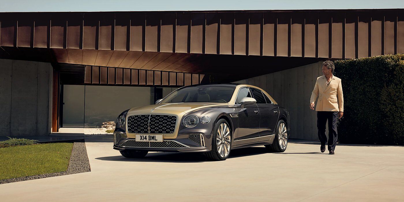 Bentley Edinburgh Bentley New Flying Spur Mulliner V8 hybrid sedan front three quarters in Rose Gold over Magnetic paint, parked near modern home