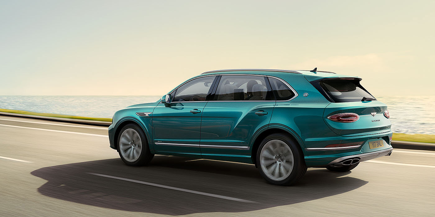 Bentley Edinburgh Bentley Bentayga Extended Wheelbase Azure luxury SUV rear three quarter in Topaz Blue by Mulliner paint, driving on an ocean road.