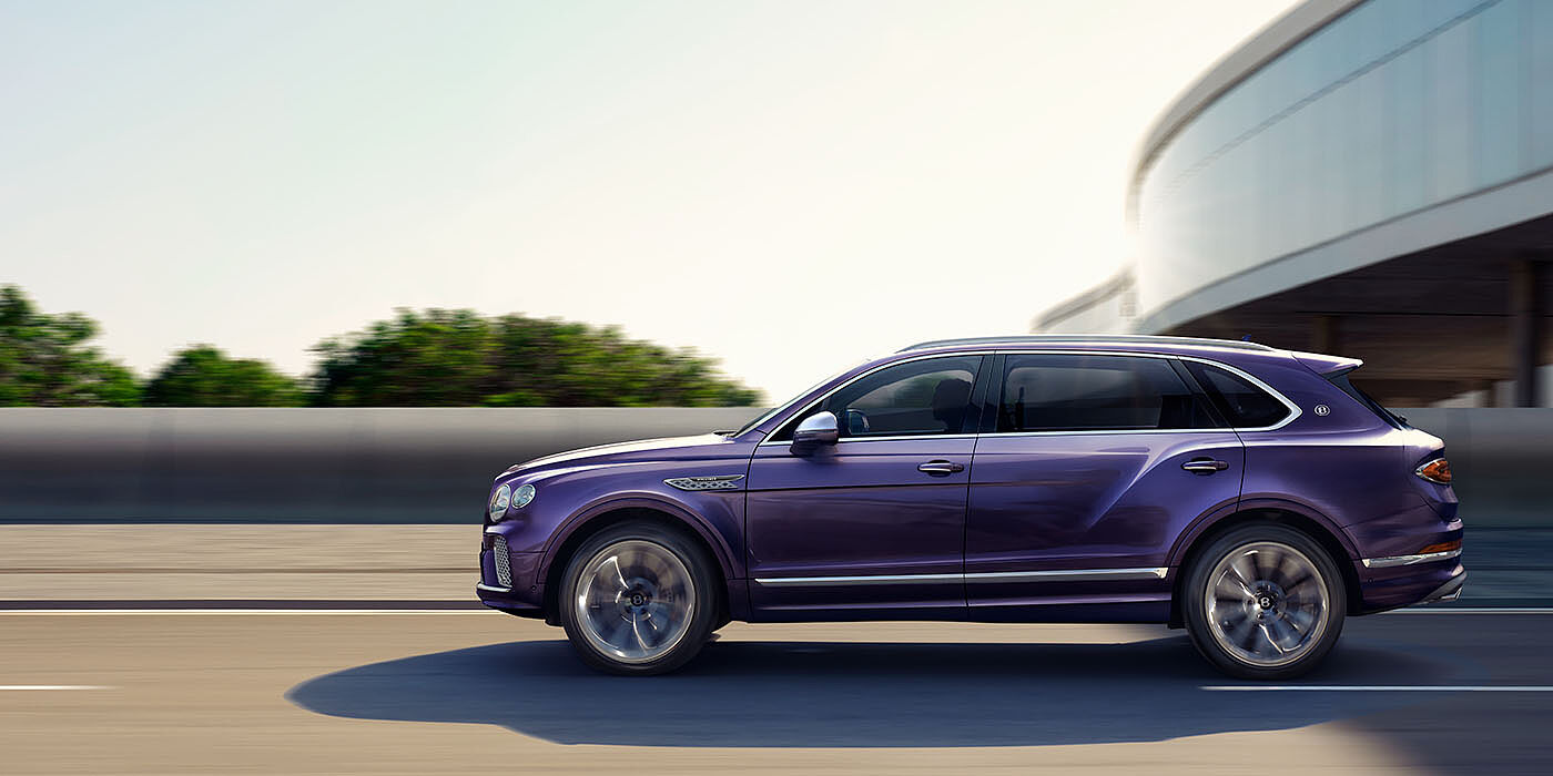 Bentley Edinburgh Bentley Bentayga Extended Wheelbase Mulliner luxury SUV profile in Tanzanite Purple paint, driving on an country road past trees.