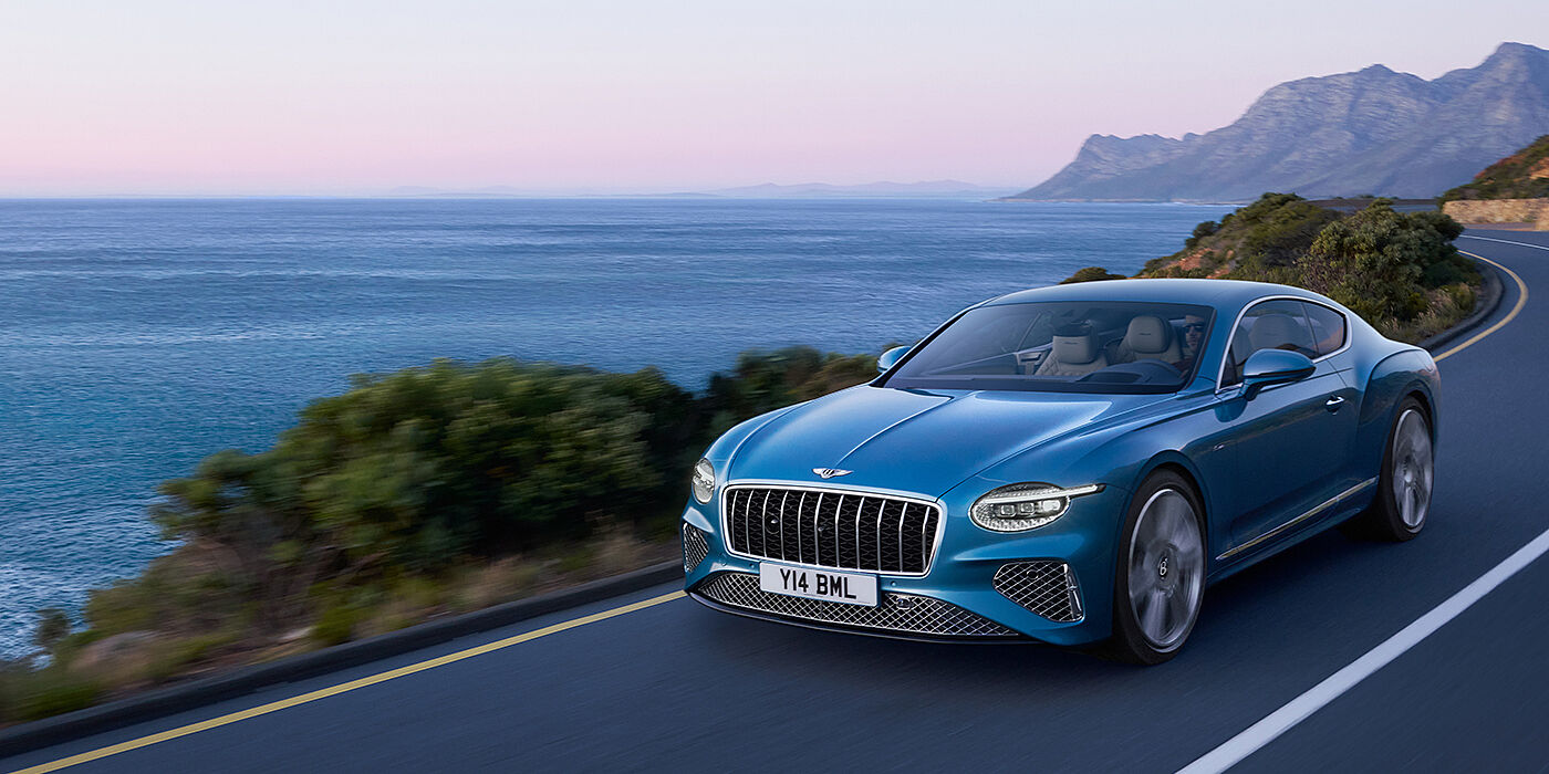 Bentley Edinburgh New Bentley Continental GT Azure coupe in Light Windsor blue paint with 22 inch Azure wheels and chrome grill, driving dynamically by the sea