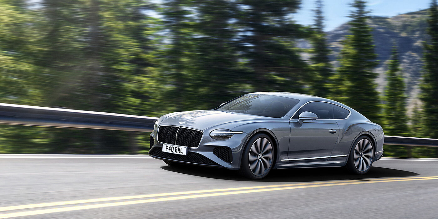 Bentley Edinburgh New Bentley Continental GT coupe in Silverlake paint and 22 inch ten-spoke wheels, driving dynamically on a tree-lined road in the sunshine