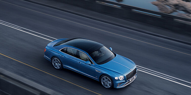 Bentley Edinburgh New Bentley Flying Spur Azure sedan in Light windsor blue paint by Mulliner, with 22 inch Azure wheels seen from overhead driving dynamically on a country road