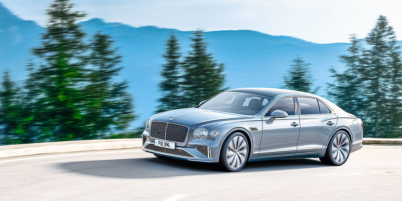 Bentley Edinburgh New Bentley Flying Spur sedan side view in Silverlake paint with ten spoke wheels and chrome matrix grille driving dynamically on a mountain road