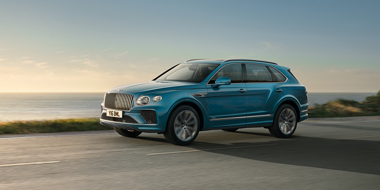 Bentley Edinburgh Bentley Bentayga Azure SUV in Topaz blue paint driving dynamically by the ocean with 22 inch 10 spoke directional wheels