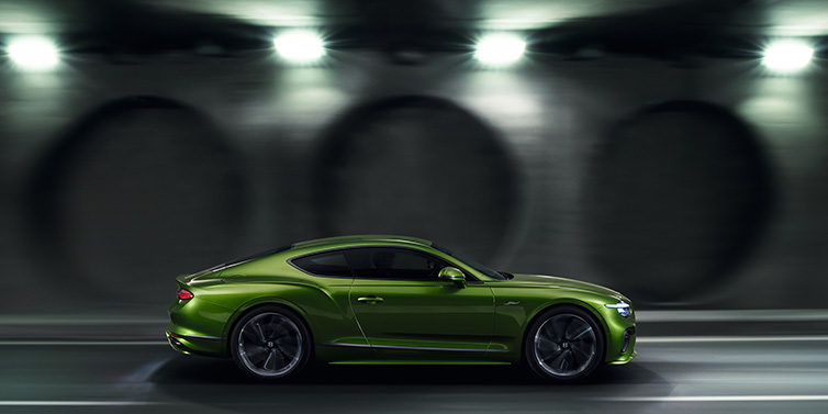 Bentley Edinburgh Bentley Continental GT Speed coupe profile in Tourmaline Green driving dynamically past a concrete wall at night