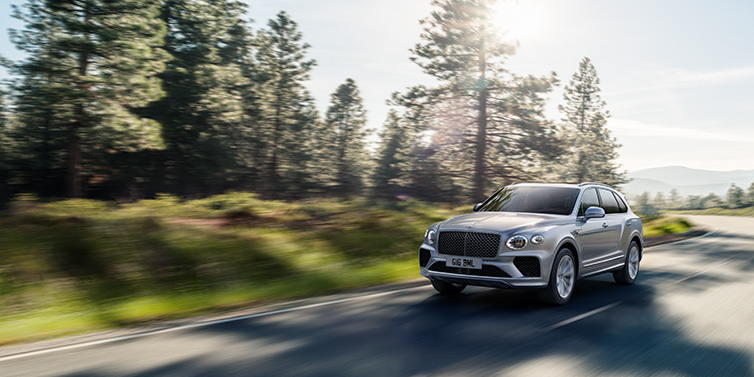 Bentley Edinburgh Bentley Bentayga SUV front three quarter in Moonbeam silver paint driving dynamically along a tree-lined road