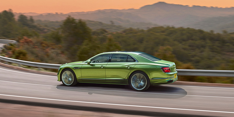 Bentley Edinburgh Bentley Flying Spur Speed sedan side profile in Tourmaline Green paint driving dynamically on a mountain road at sunset