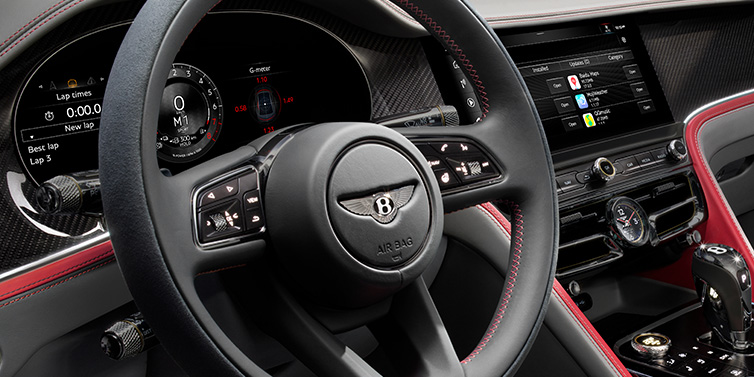 Bentley Edinburgh Bentley Flying Spur Speed sedan front interior detail showing steering wheel and driver screens surrounded with Hotspur red and Gravity Grey hides